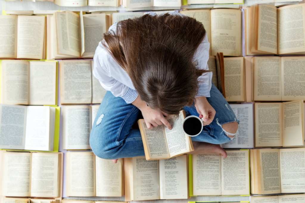 Femme assise entourée de livres, prenant des notes tout en buvant du café, illustrant la phase d’analyse pour une fiche de lecture.