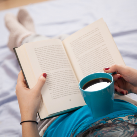 Personne lisant un livre avec une tasse de café, idéale pour compléter son carnet de lecture.