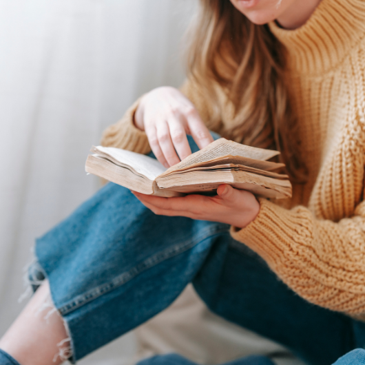 Comment faire une fiche de lecture d’un livre ? 2 Jeune femme en pull jaune concentrée sur sa lecture, étape essentielle pour rédiger une fiche de lecture.