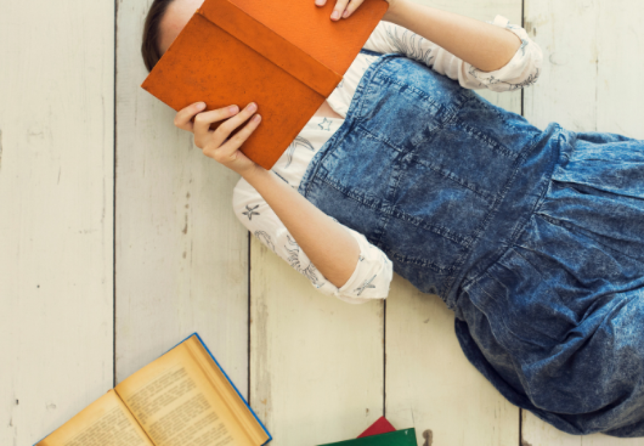 Femme allongée lisant un livre, entourée d'autres ouvrages pour enrichir son carnet de lecture.