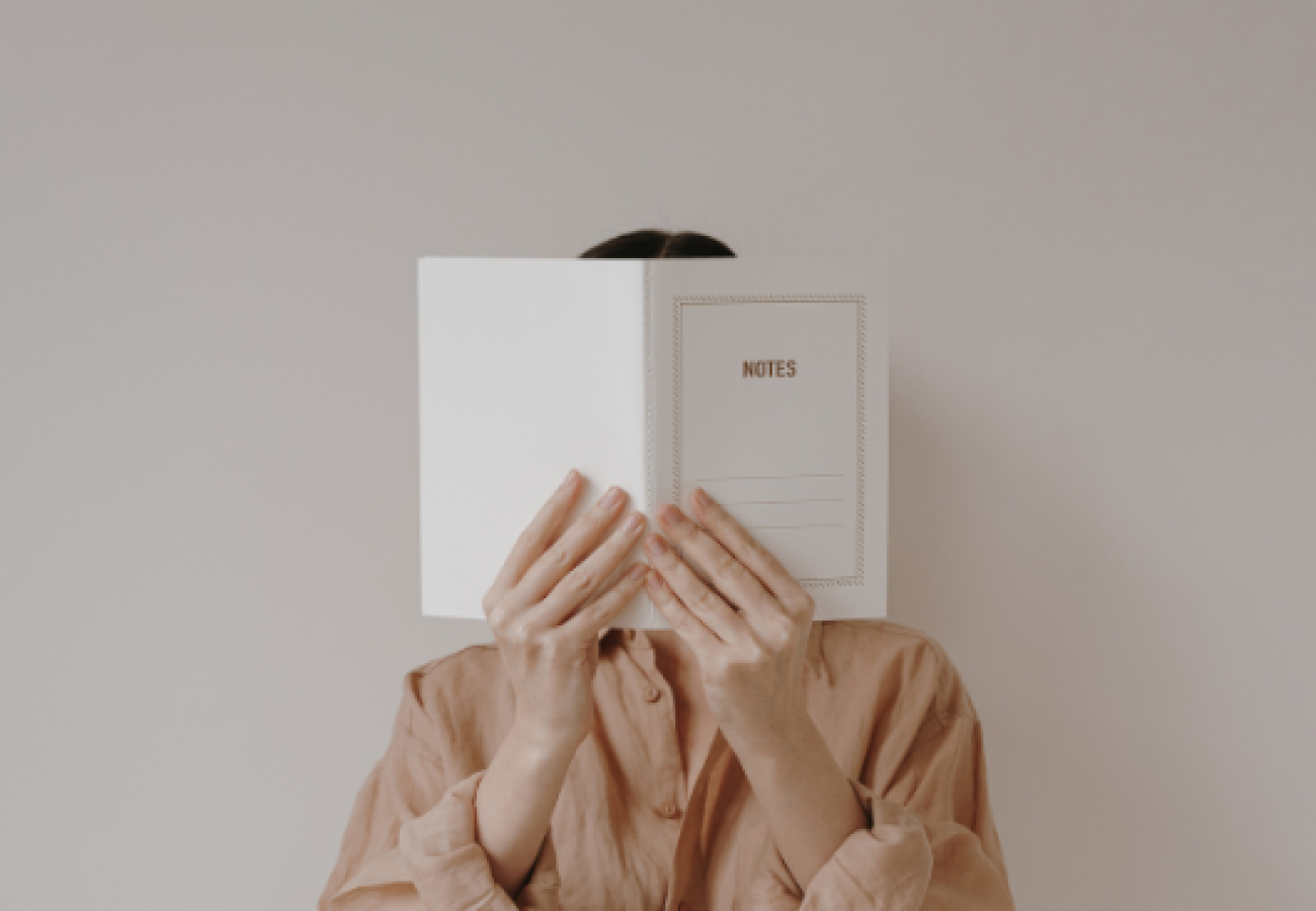 Femme tenant un carnet blanc marqué "notes", prête à commencer son journal de lecture